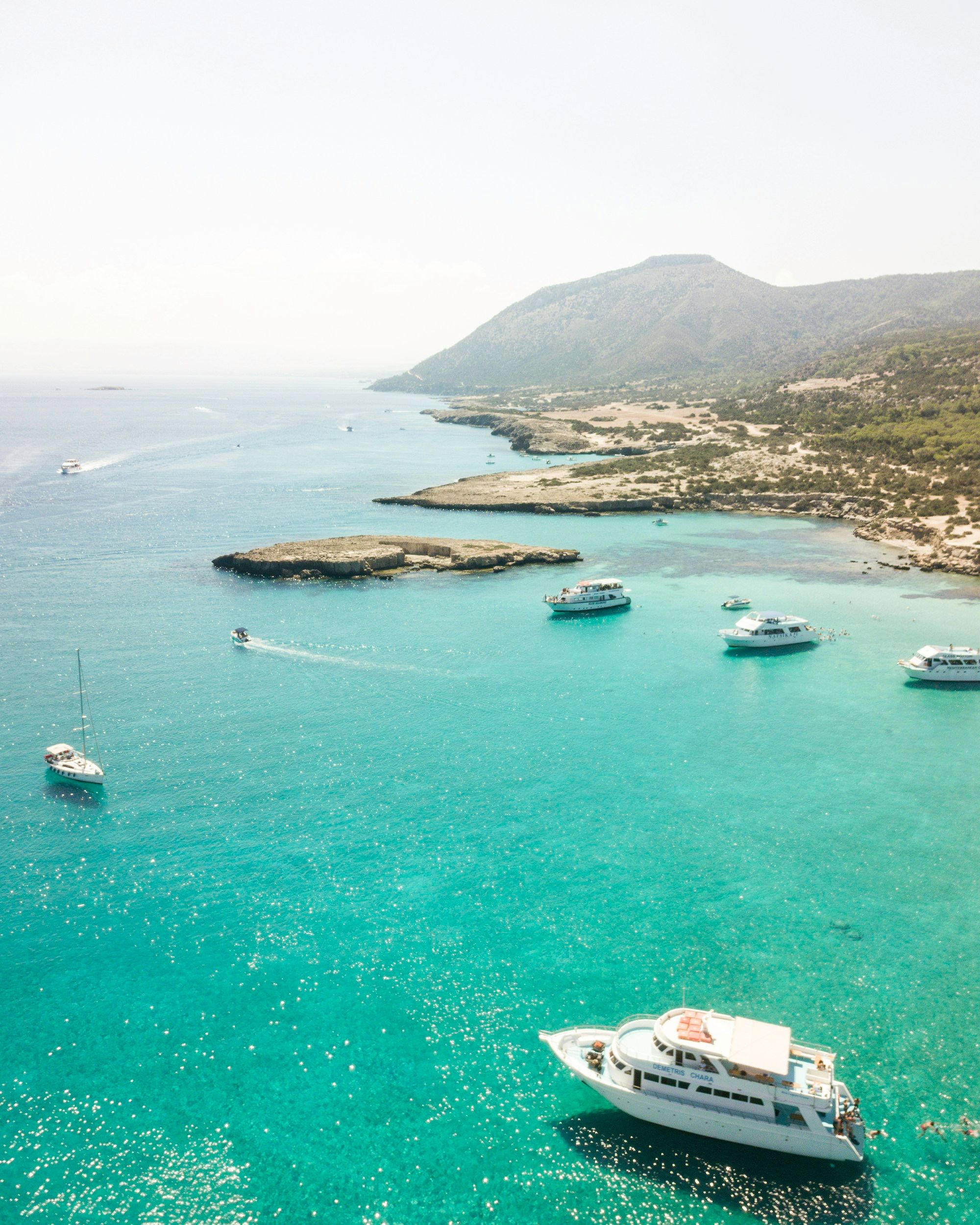 Boats at anchor in a turquoise bay beneath the hills of the Akamas peninsula.