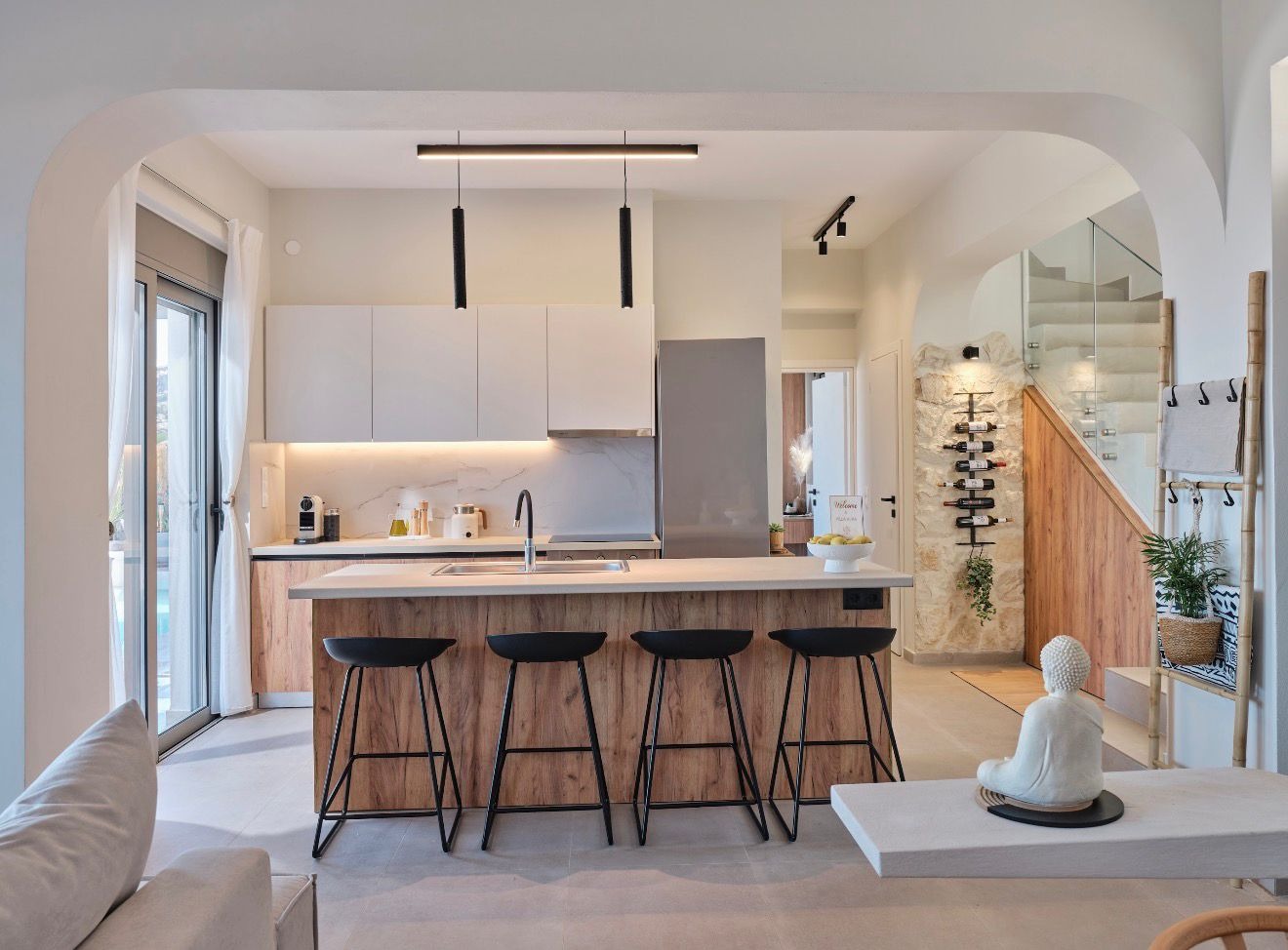 An open kitchen with a wood-fronted island and four black stools, framed by a curved white arch.
