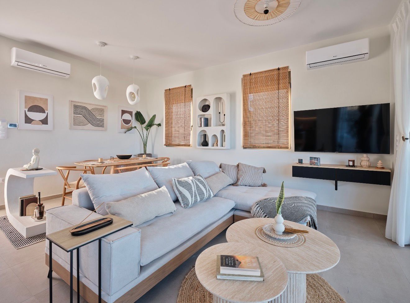 A bright living room with a pale corner sofa, travertine coffee tables and bamboo blinds.